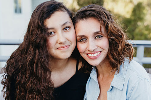 mother and daughter with their heads leaning on each other, looking at camera and smiling.